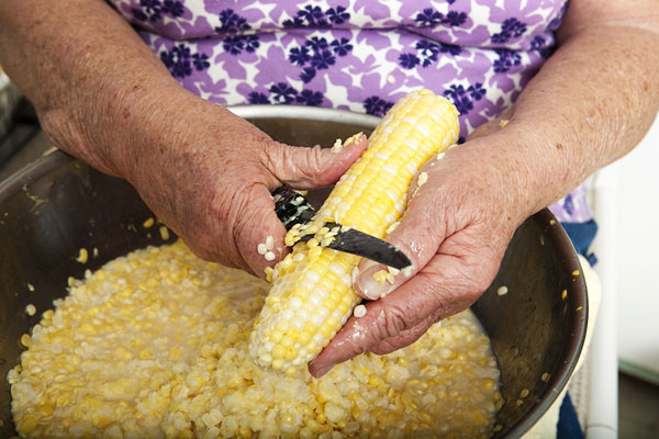 Alice Blanton demonstrates the skillful first pass of her sharpened blade over a corn cob. The first pass is the most important as it unleashes the creaminess that will be the hallmark of her cream-style corn.